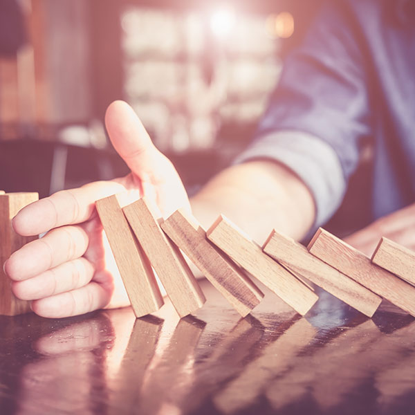 One person holds a hand between dominoes to stop the domino effect. | Credit risis: Protect yourself against bad debts with NW Assekuranz.