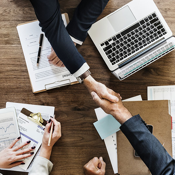 Draufsicht auf zwei Personen, die Hände schütteln über einem Meeting-Tisch | Maßgeschneiderte M&A-Versicherungen mit NW Assekuranz