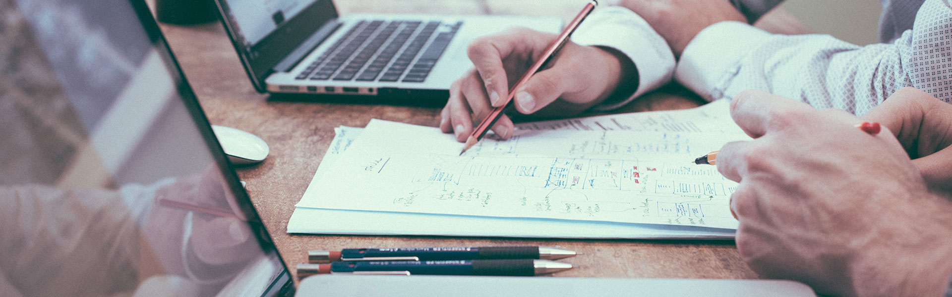 Close-up of sheet of paper on a table with two people talking about it | Insurance management by NW Assekuranz